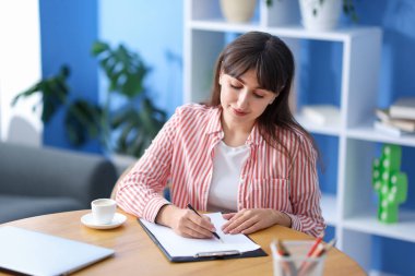Kahve molası. Güzel bir kadın, kapalı bir masada, bardağın yanında yazıyor.