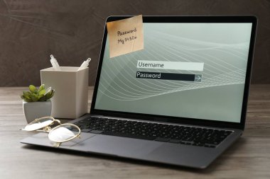 Şifreli dizüstü bilgisayar, kullanıcı adı, kağıt not, gözlük ve kırtasiye malzemesi ahşap masada.