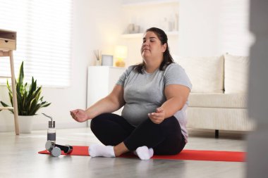Evde yoga minderi üzerinde meditasyon yapan şişman kadın.