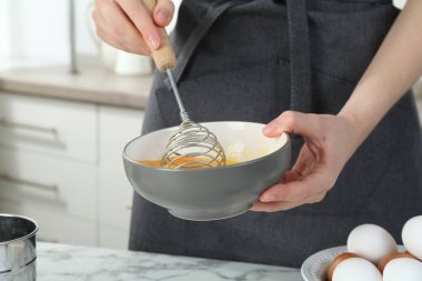 Mutfaktaki beyaz mermer masada çırpılmış yumurta çırpan kadın, yakın plan.