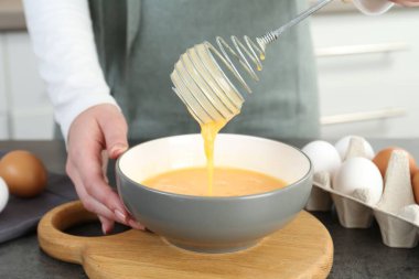 Mutfaktaki gri masada çırpılmış yumurta çırpan kadın, yakın plan.