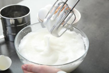 Gri masada yumurta beyazını mikserle döven kadın, yakın plan.