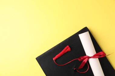 Sarı arka planda diploma ve mezuniyet şapkası, üst manzara. Metin için boşluk