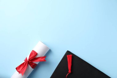 Açık mavi arka planda diploma ve mezuniyet şapkası, düz yatış. Metin için boşluk