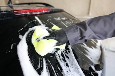 Oto yıkayan adam araba yıkamada süngerle yıkıyor.