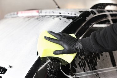 Oto yıkayan adam araba yıkamada süngerle yıkıyor.