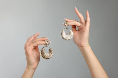 Gri arka planda zarif küpeleri olan kadın, yakın plan.