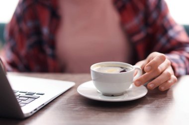 Kahve molası. Bir fincan aromatik içeceği ve laptopu olan kadın ahşap masada, yakın plan.