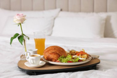 Nefis bir kahvaltı tepsisi ve otel odasında yatakta gül, yakın plan. Metin için boşluk