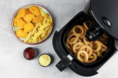 Lezzetli kalamar halkalı kızartma, tavuk nugget, patates kızartması ve soslar gri masada, düz yerde.