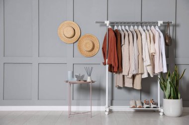 Askıda asılı kadın kıyafetleri, şapkalar, ev bitkisi ve dekorlu kahve masası. Kapalı gri duvarın yanında. Metin için boşluk