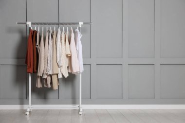 İçerideki gri duvarın yanında farklı kıyafetler asılı. Metin için boşluk