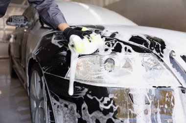 Oto yıkayan adam araba yıkamada süngerle yıkıyor.