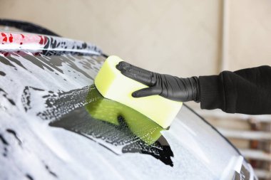 Oto yıkayan adam araba yıkamada süngerle yıkıyor.