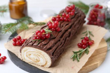 Lezzetli Noel kütüğü (geleneksel Noel pastası) beyaz masa üzerinde kırmızı frenk üzümü, yakın plan