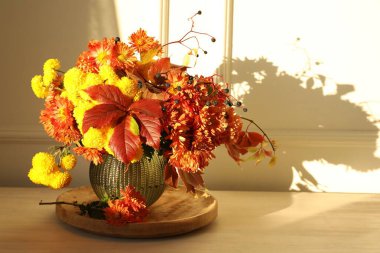 Sonbahar atmosferi. Üzerinde güzel çiçekler ve böğürtlenler olan vazo, ışık duvarının yanındaki ahşap masada, metin için yer var.