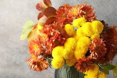 Sonbahar atmosferi. Güzel çiçekli vazo ve gri duvarın yanında yapraklar, yakın plan.