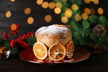 Noel yemeği. Lezzetli Panettone pastası, malzemeler ve ahşap masanın üzerindeki dekoratif dekor arka planda bulanık ışıklar, yakın plan. Bokeh etkisi