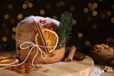 Noel yemeği. Lezzetli Panettone pastası, malzemeler ve arka planda arka planda bulanık ışıklı şenlikli dekor, yakın plan. Bokeh etkisi