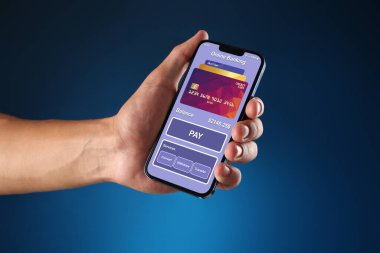 Çevrimiçi ödeme. Elinde cep telefonu olan mavi arka planda uygulaması açık bir adam, yakın plan.