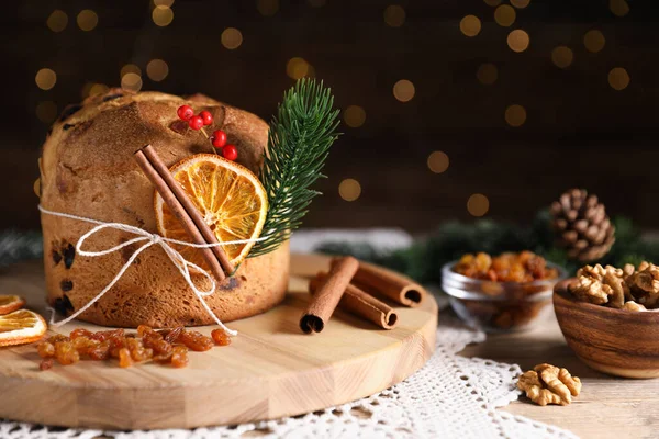Noel yemeği. Lezzetli Panettone pastası, malzemeler ve ahşap masanın üzerindeki dekoratif dekor arka planda bulanık ışıklar, yakın plan. Bokeh etkisi