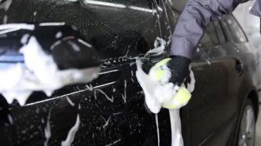 Oto yıkayan adam araba yıkamada süngerle yıkıyor.