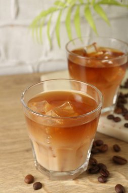 Lezzetli buzlu kahve, bardakta süt, ahşap masada fasulye, arka planda hafif desenli, yakın plan.