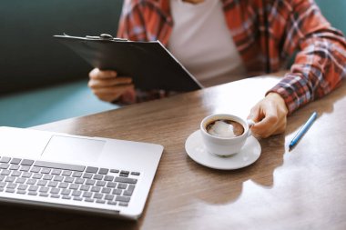 Kahve molası. Elinde bir bardak aromatik içecek ve tahta pano olan bir kadın, kapalı bir masa, yakın plan.