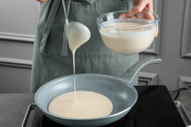 Mutfaktaki gri masada kaseden tavaya sıvı hamur döken kadın, yakın plan.