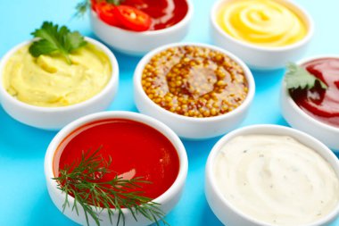 Açık mavi masada farklı soslar ve otlar, yakın plan.