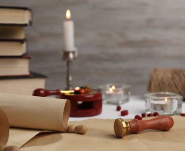 Eski parşömen kağıdı, balmumu damgası, mühür kaşığı, kitaplar ve yanan mumlar.