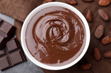 Erimiş çikolatalı kase, fasulye ve parçalar gri masada, düz yerde.