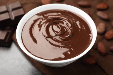 Erimiş çikolatalı kase, fasulye ve parçalar gri masada, yakın plan.