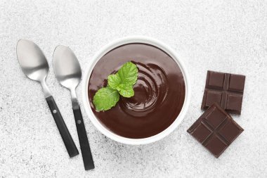 Erimiş çikolata kasede nane, parçalar ve kaşıklar açık gri masada, düz yatıyordu.