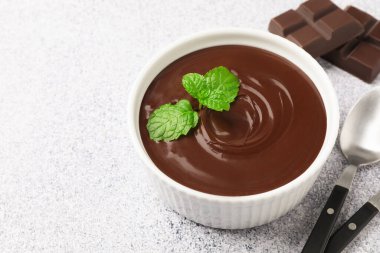 Erimiş çikolata, kasede nane şekeri, parçalar ve açık gri masada kaşık, yakın plan. Metin için boşluk