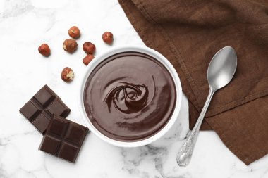 Erimiş çikolata kasede, parçalarda, fındıkta ve kaşıkta beyaz mermer masada, düz yerde.