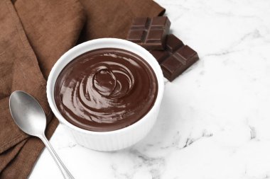 Erimiş çikolata kasede, parçalar ve kaşık beyaz mermer masada, yakın plan. Metin için boşluk