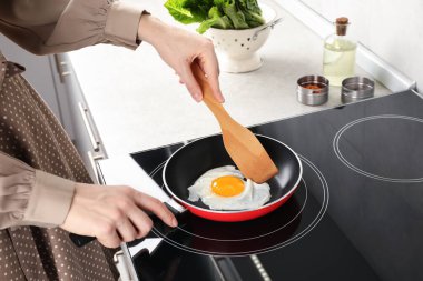 Mutfakta ahşap spatulayla sahanda yumurta yiyen bir kadın. Yakın plan.