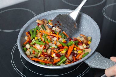 Kızartma tavasında taze sebze ve spatula karıştıran kadın, yakın plan.