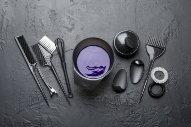 Tabaktaki saç boyama ürünü ve siyah masada farklı kuaför aletleri, düz yatış.