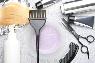 Tabaktaki saç boyama ürünü, bir tutam saç ve açık gri masada farklı kuaför aletleri.