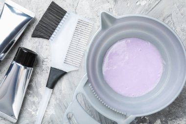 Tabaktaki saç boyama ürünü ve açık gri masada farklı kuaför aletleri.