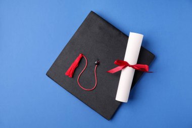 Mavi arka planda diploma ve mezuniyet şapkası, üst görünüm