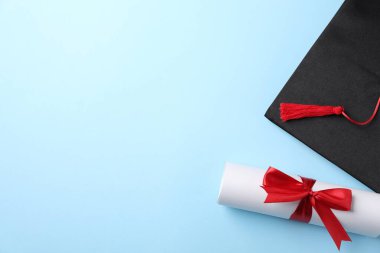 Açık mavi arka planda diploma ve mezuniyet şapkası, düz yatış. Metin için boşluk