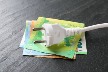 Fişi ve avro banknotları olan elektrik teli siyah masa üzerinde, yakın plan