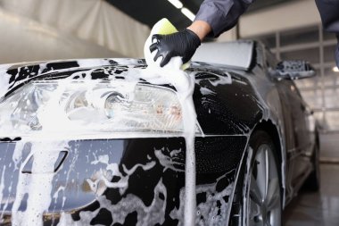 Oto yıkayan adam araba yıkamada süngerle yıkıyor.