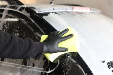 Oto yıkayan adam araba yıkamada süngerle yıkıyor.