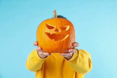 Cadılar Bayramı kutlaması. Açık mavi arka planda oyulmuş ürkütücü yüzlü bir adam balkabağı tutuyor.