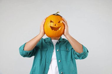 Cadılar Bayramı kutlaması. Açık gri arka planda oyulmuş ürkütücü yüzü olan bir adam balkabağı tutuyor.