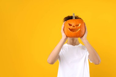 Cadılar Bayramı kutlaması. Turuncu arka planda oyulmuş ürkütücü yüzlü çocuk balkabağı tutuyor, mesaj atmak için yer var.